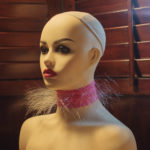 A photograph documenting the artwork Throat Apparatus. The apparatus is a piece of pink, elastic fabric with hundreds of clear monofilament threads emerging from it like hair. This strip is worn tight as a collar, giving the effect of a cloud of hairs around the neck. It is pictured here on a mannequin.